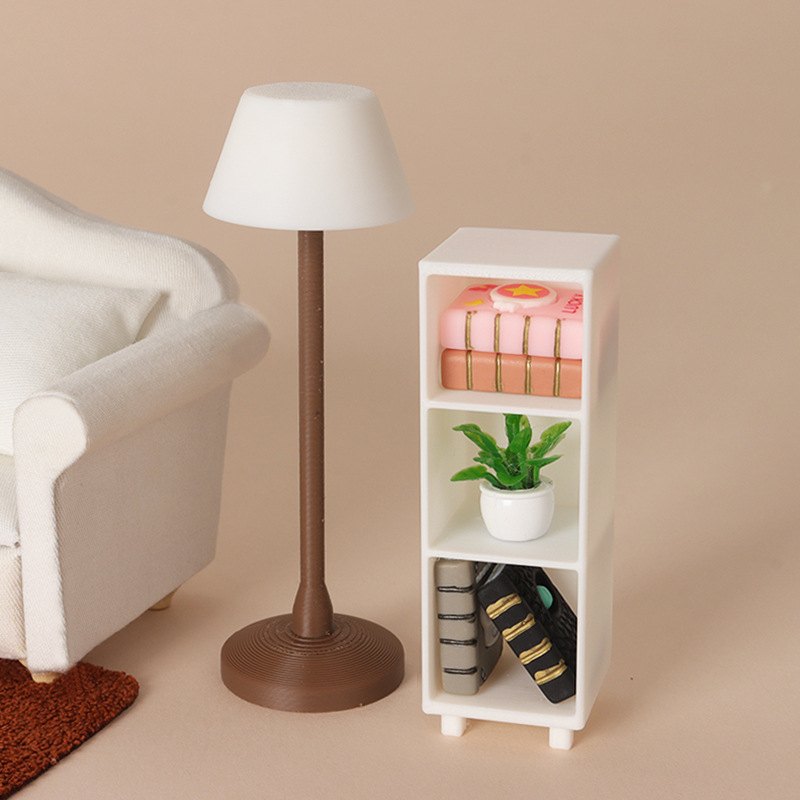 Miniaturowa lampa z brązową nóżką obok kremowej sofy i regału z książkami