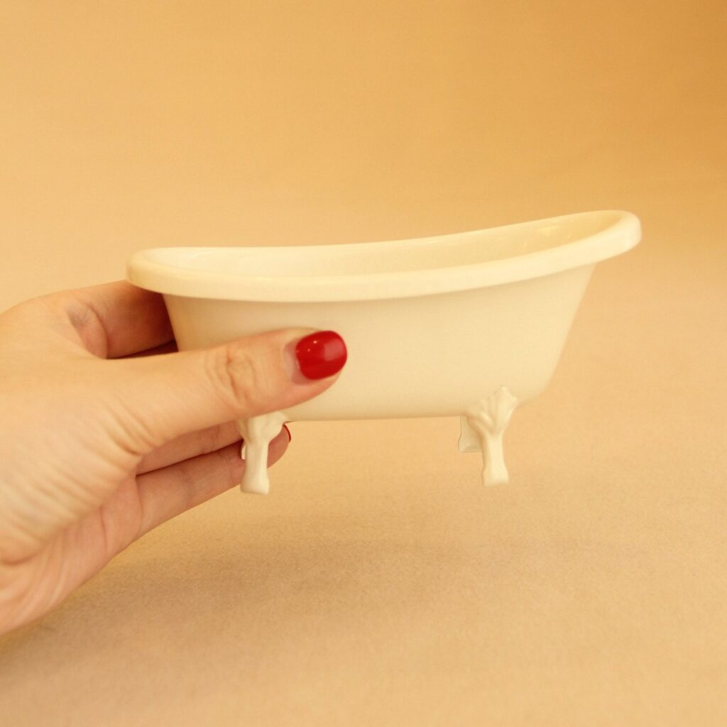 Miniaturowa wanna na nóżkach trzymana w dłoni dla pokazania skali